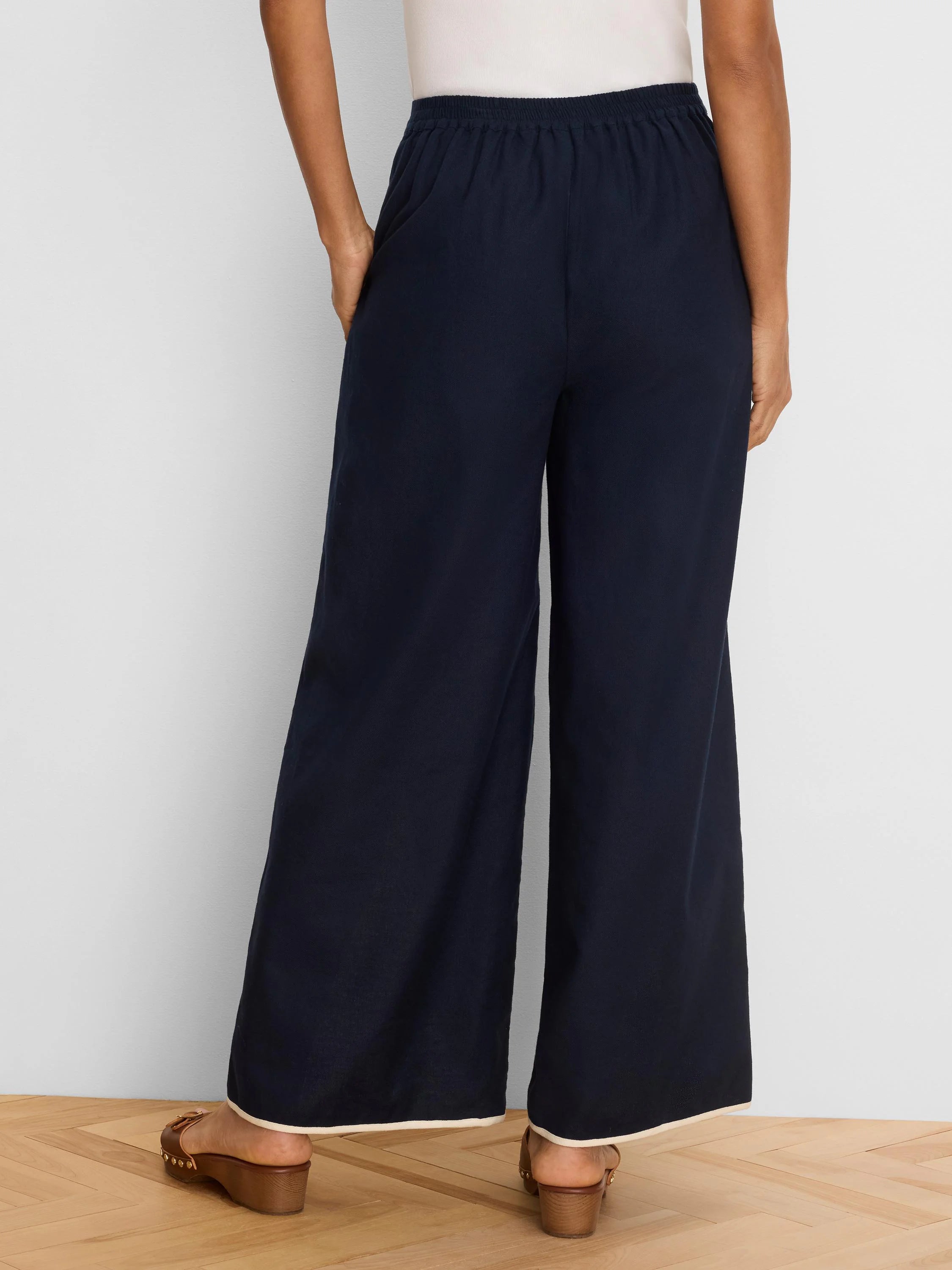 Rear view of navy wide leg pants with an elasticized waist and light-colored piping along the hem.