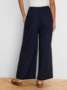 Rear view of navy wide leg pants with an elasticized waist and light-colored piping along the hem.