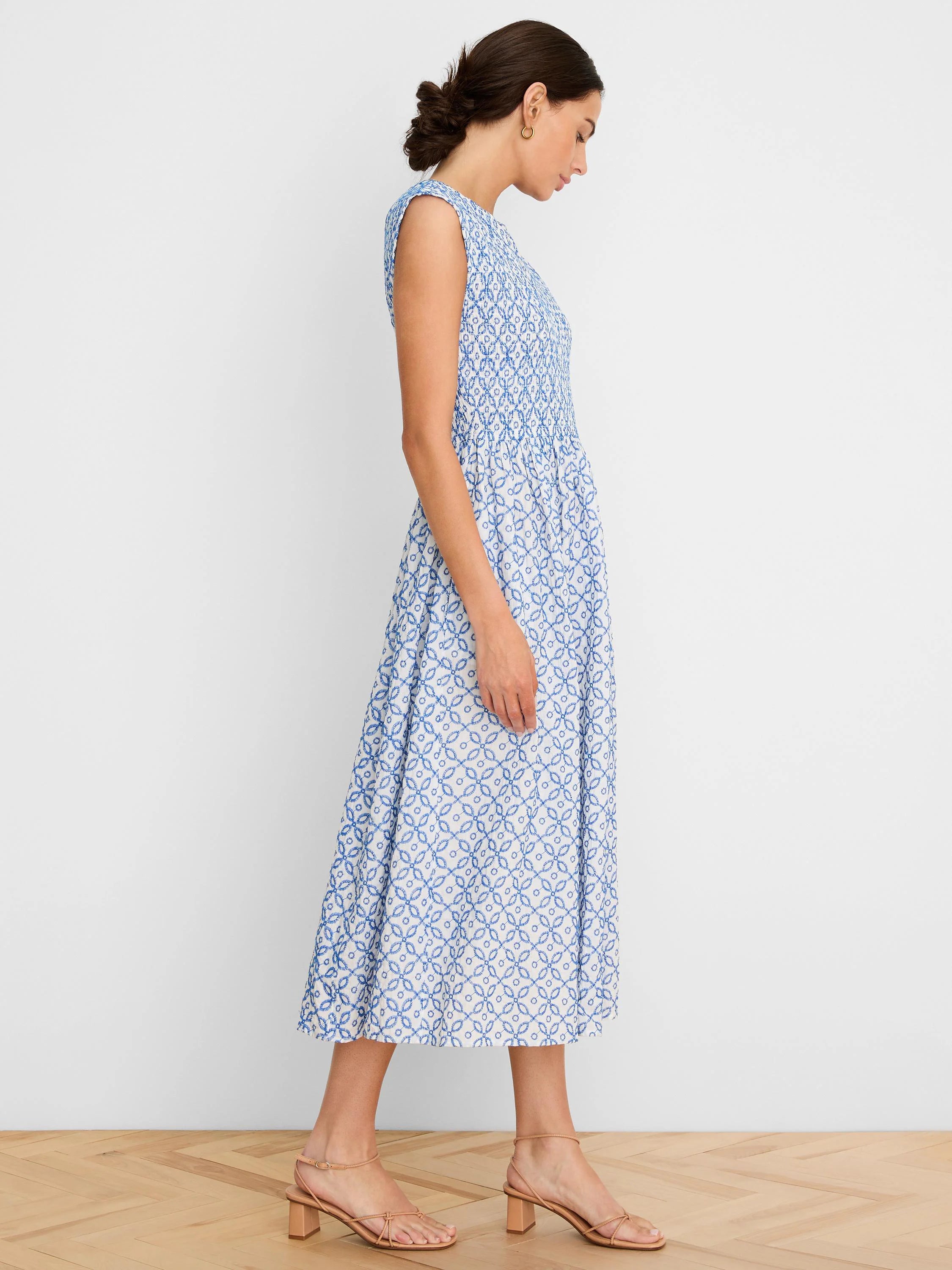 White midi dress with blue embroidered geometric tile pattern, sleeveless and smocked bodice.