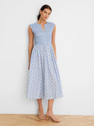 White sleeveless dress with blue tile pattern. Notched V-neck, smocked bodice, A-line midi skirt.