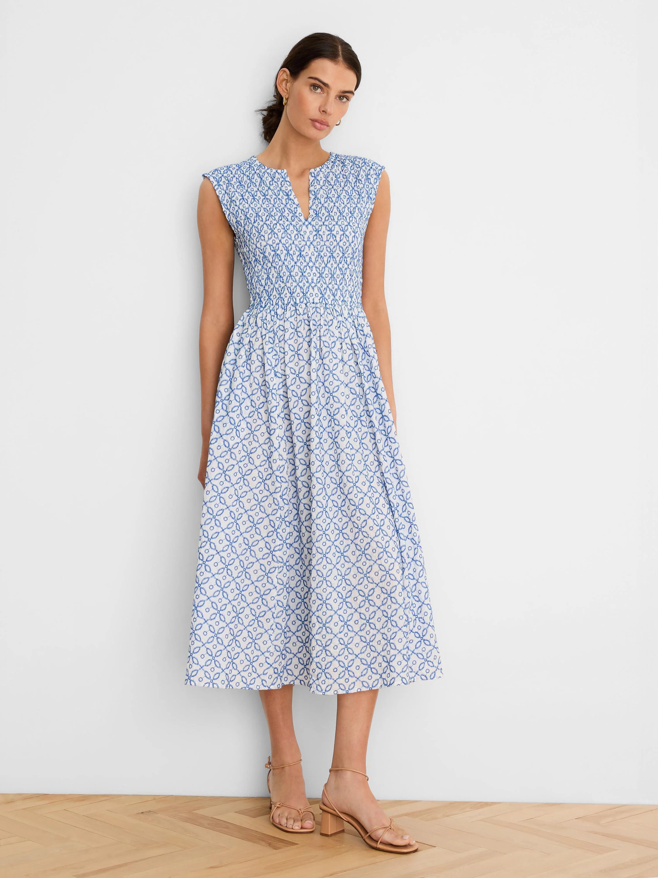 White sleeveless dress with blue tile pattern. Notched V-neck, smocked bodice, A-line midi skirt.