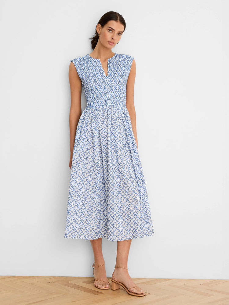 White sleeveless dress with blue tile pattern. Notched V-neck, smocked bodice, A-line midi skirt.