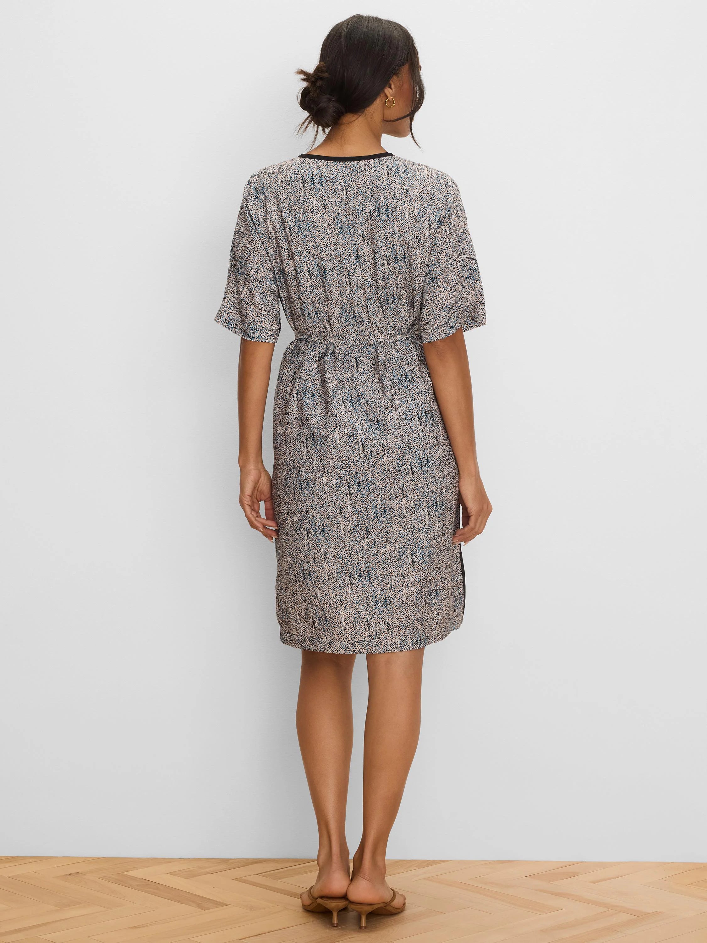Short-sleeved, knee-length dress with a beige and blue speckled pattern and black neckline trim. Belted waist.