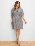 Knee-length dress with beige, blue, and black speckled pattern, short sleeves, V-neck with black trim, and tie waist.