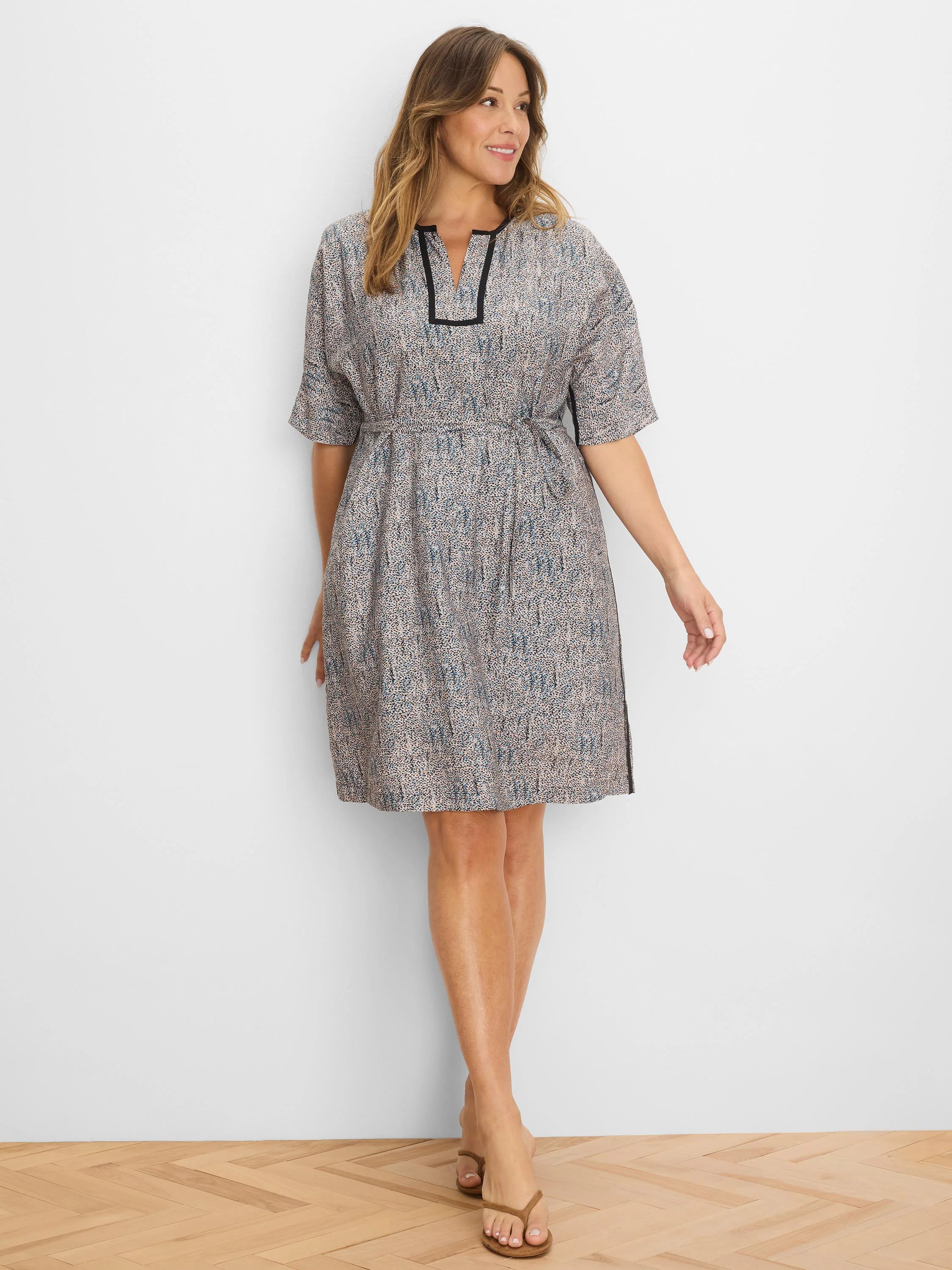 Knee-length dress with beige, blue, and black speckled pattern, short sleeves, V-neck with black trim, and tie waist.