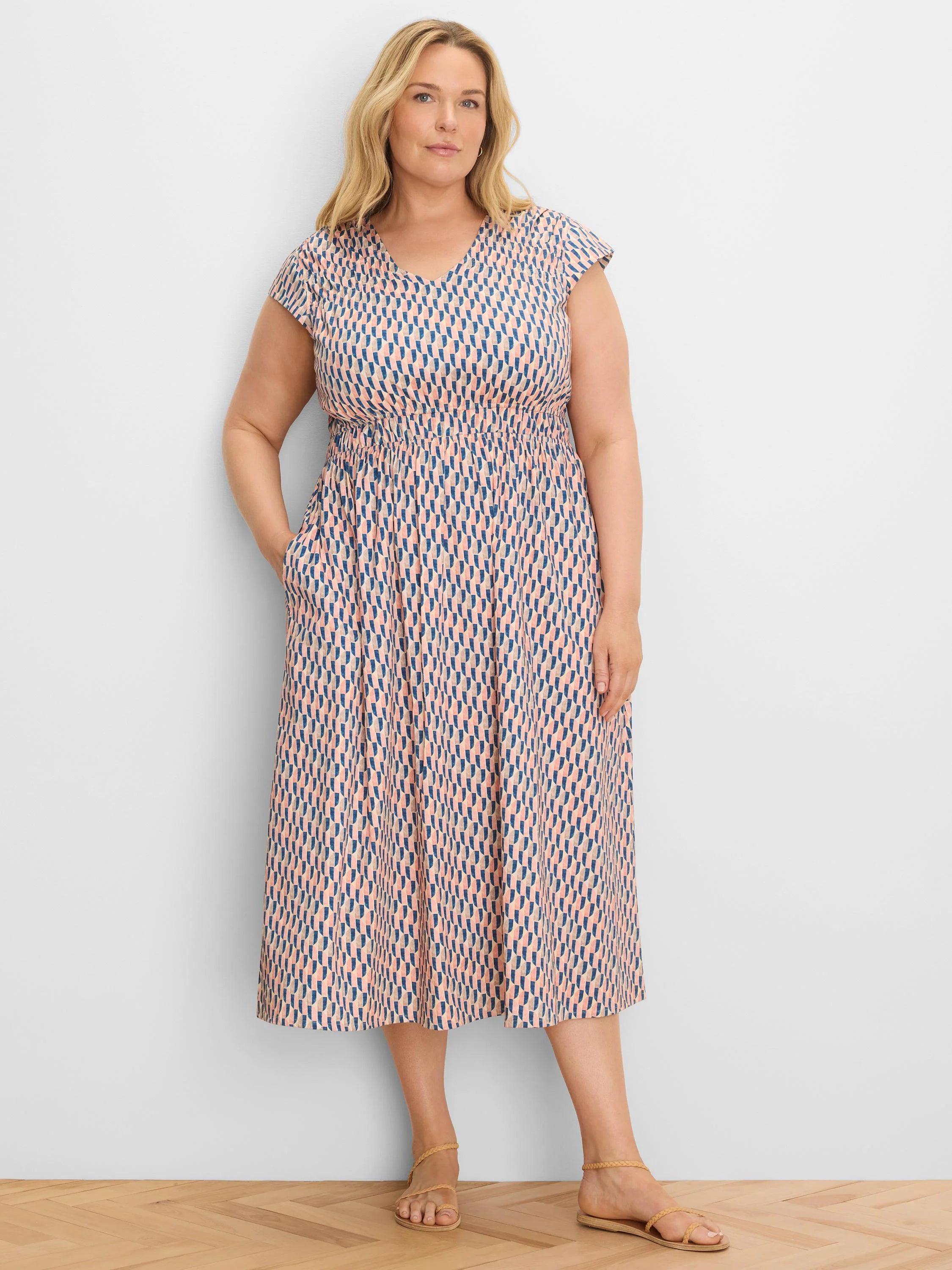 Model in peach and navy geometric print V-neck cap sleeve midi dress with smocked waist and pockets.