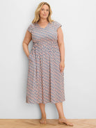 Model in peach and navy geometric print V-neck cap sleeve midi dress with smocked waist and pockets.