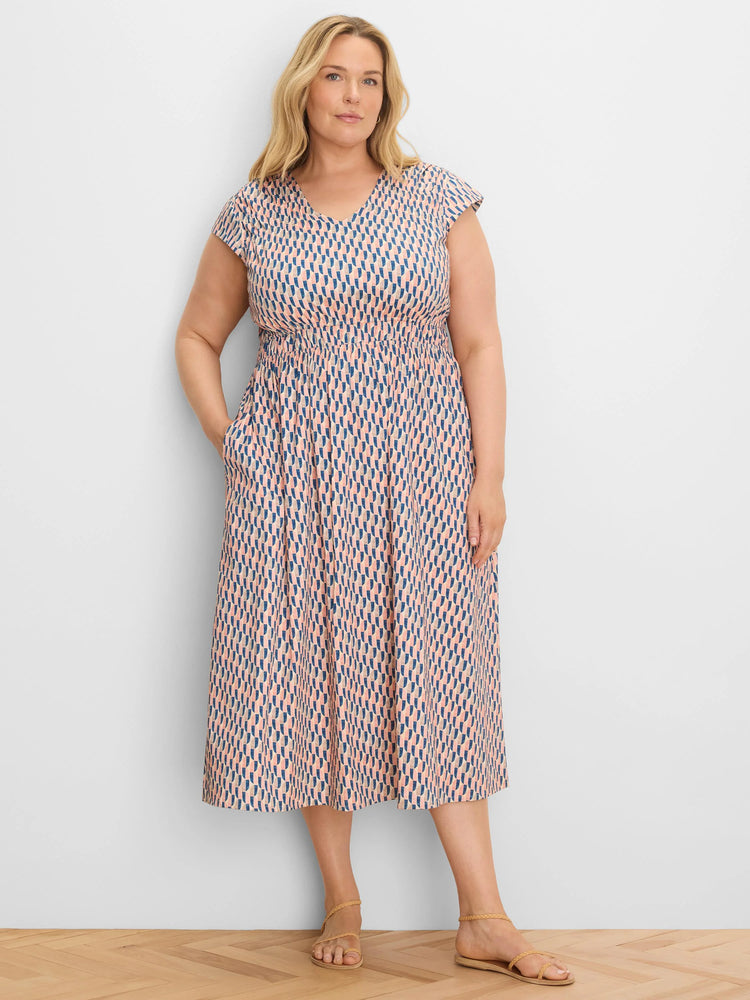 Model in peach and navy geometric print V-neck cap sleeve midi dress with smocked waist and pockets.
