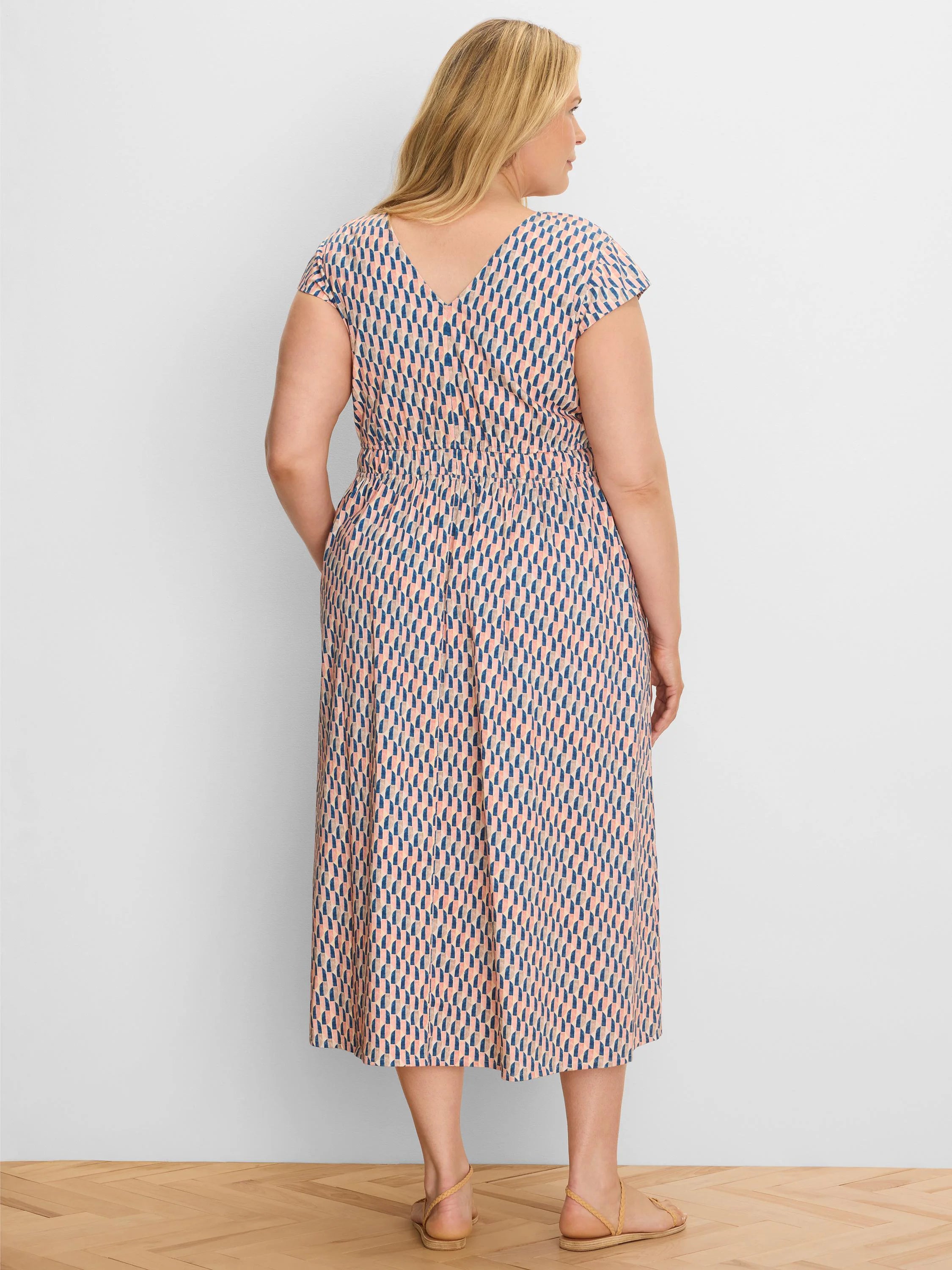 Midi dress with cap sleeves, V-back, and elasticated waist. Features a peach, navy, and tan geometric pattern.