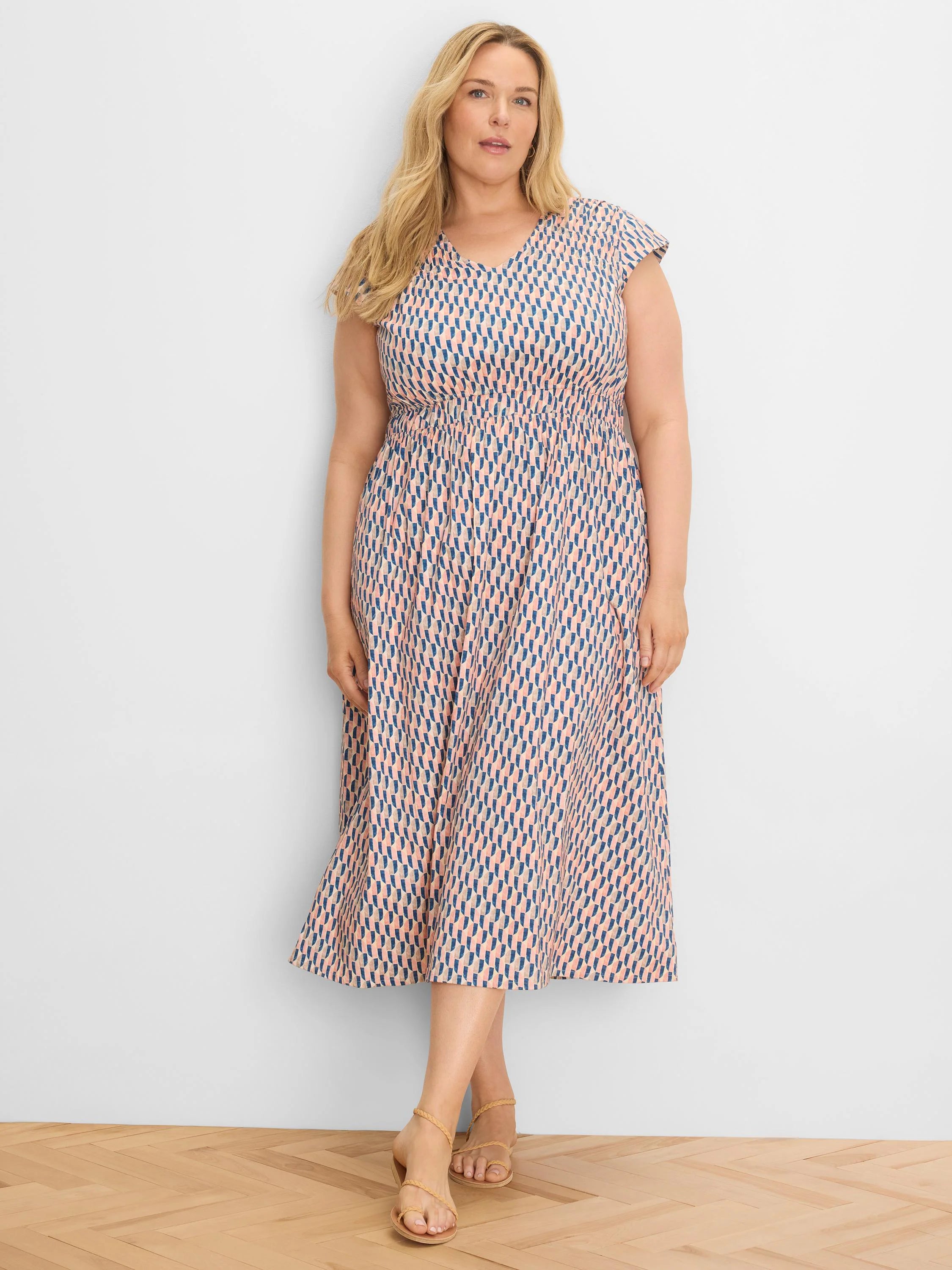 Peach V-neck midi dress with cap sleeves, shirred waist, and blue/gray geometric pattern.