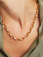 Gold chain necklace;  oval links;  worn on light skin against olive green fabric.