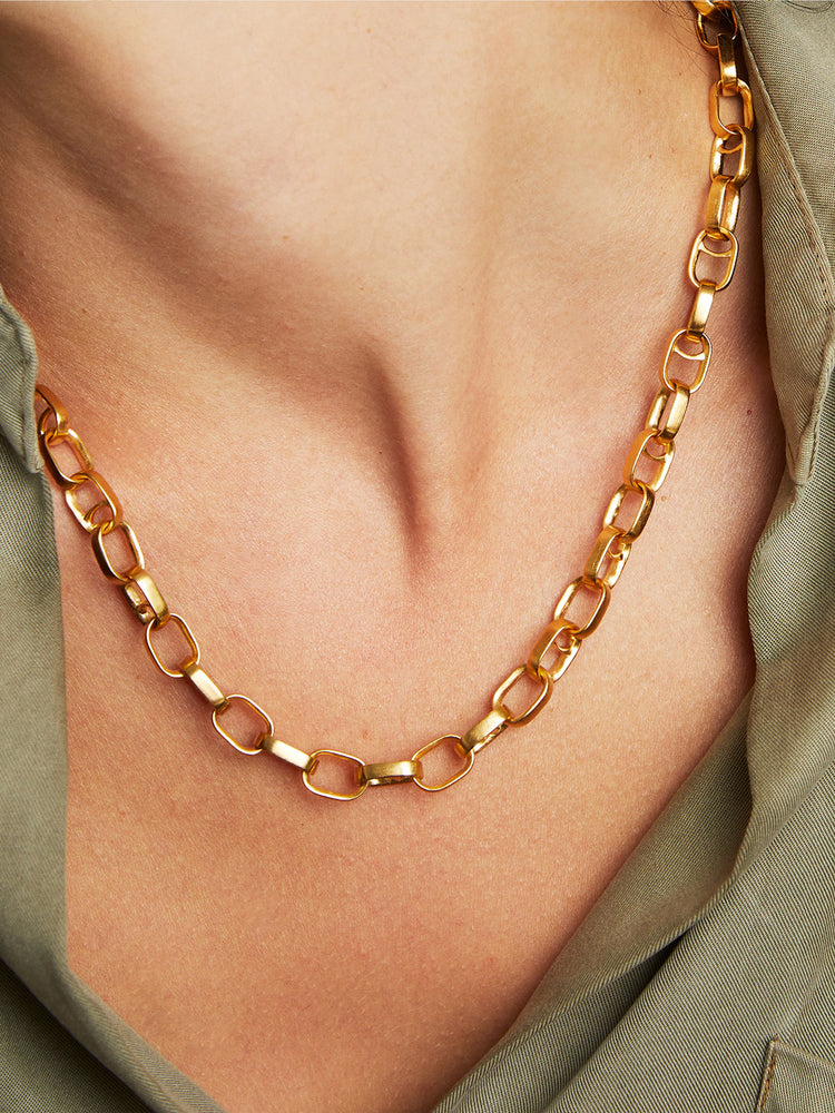 Gold chain necklace;  oval links;  worn on light skin against olive green fabric.