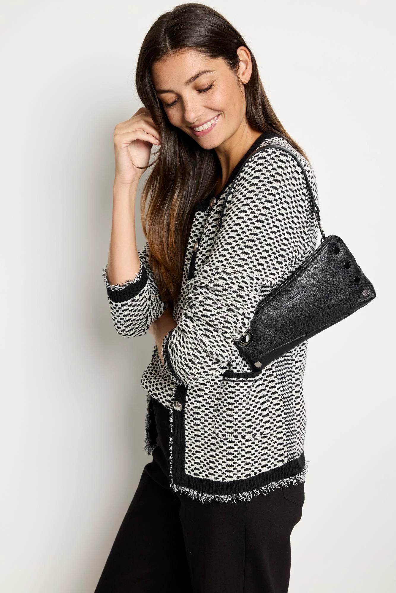 Black pebbled leather clutch, rectangular, with prominent dark metal rivets on the front and a top zipper closure.