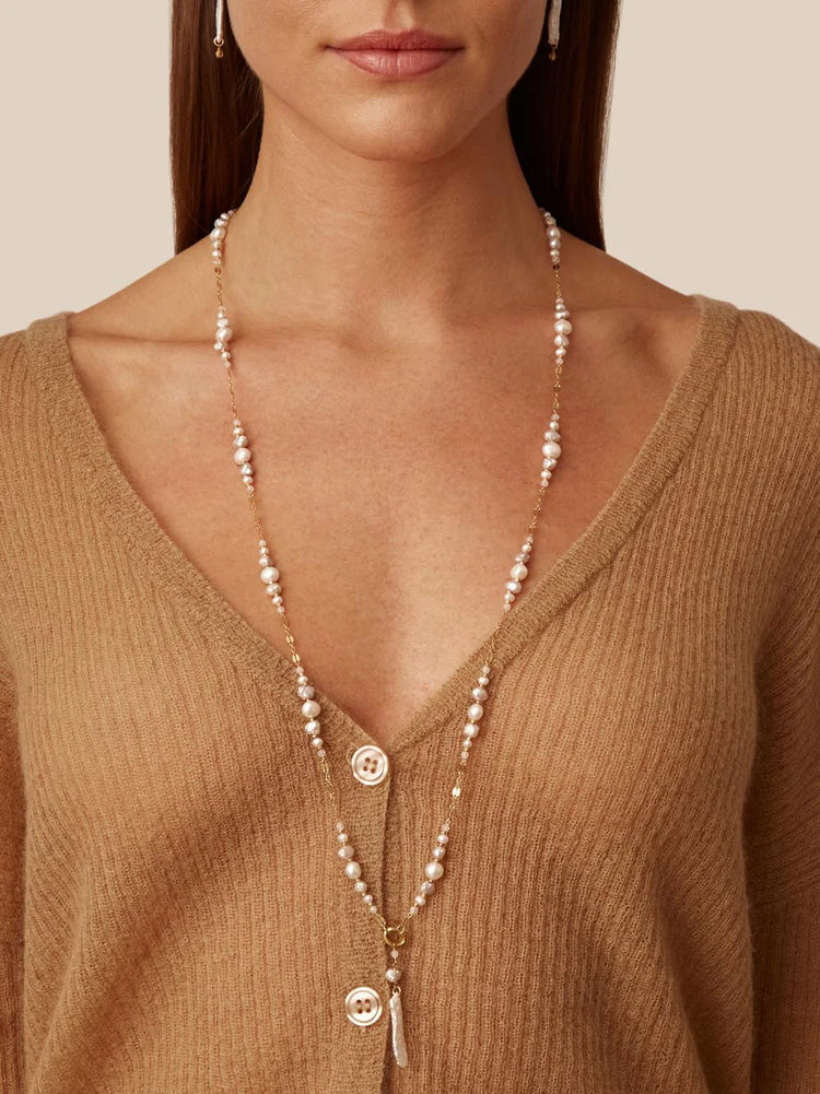 Long gold chain necklace with off-white pearls and a small, off-white, shell-shaped pendant.