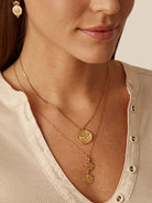 Gold necklace with a large, embossed coin-like pendant and two smaller matching charms below it on a delicate chain.