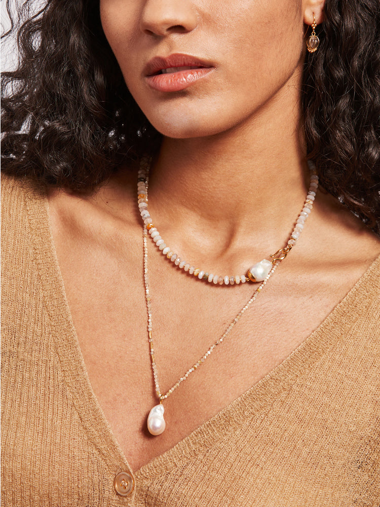 Double necklace; gold chain with small light-brown/white stones; larger, off-white baroque pearl pendant.  Second chain...