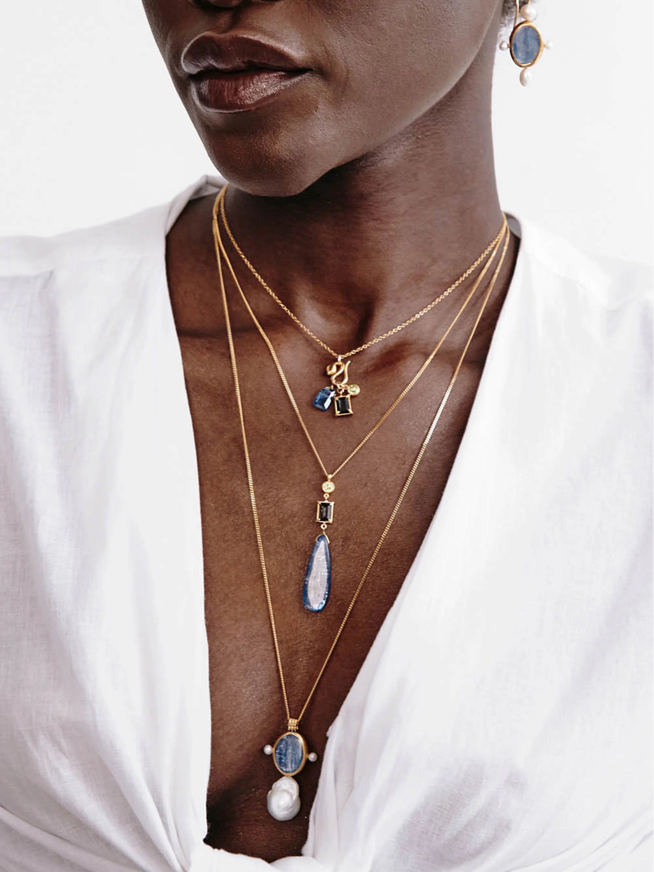 Gold layered necklaces.  Largest pendant: teardrop blue stone, white pearl, gold accents. Smaller pendants include blue,...