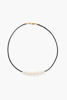 Black leather cord necklace with gold clasp, featuring six off-white pearls.