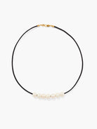 Black leather cord necklace with gold clasp, featuring six off-white pearls.