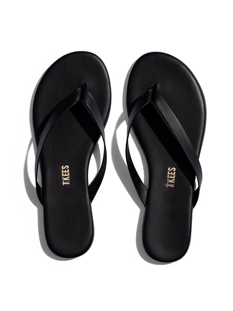 Black minimalist leather flip-flops featuring thin straps, a thin sole, and subtle gold branding on the footbed.