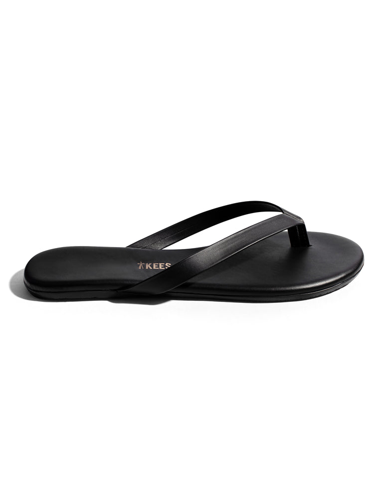 These black leather minimalist thong sandals feature a flat sole and thin, narrow crossover straps.