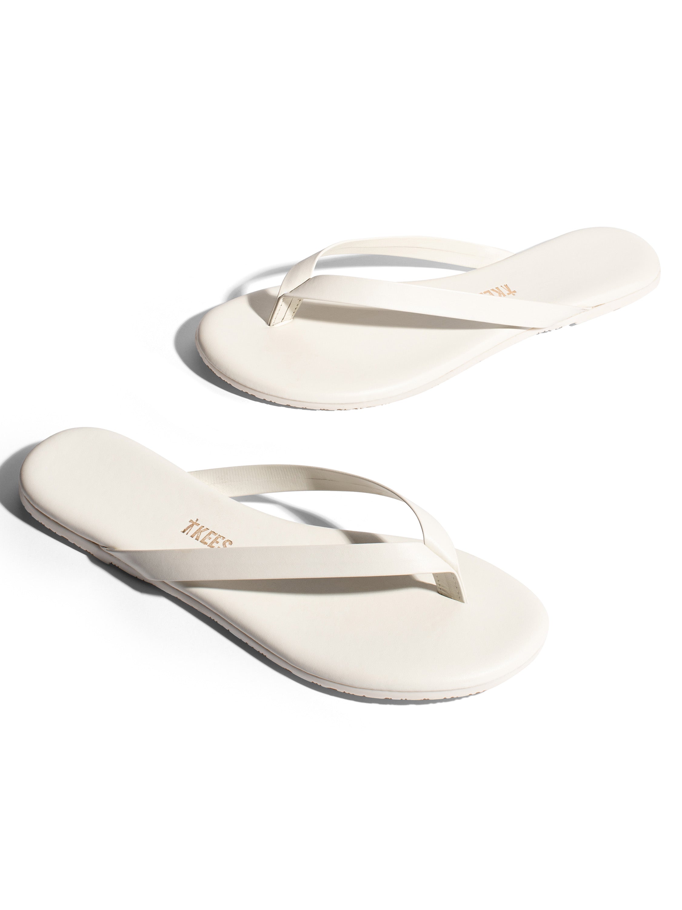 Minimalist cream leather flip-flops feature thin thong straps and a flat, casual slip-on silhouette.