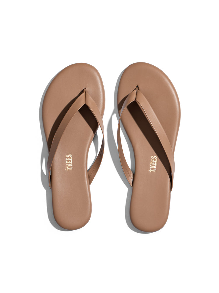 The flat, minimalist nude leather flip-flops feature thin straps and a simple, rounded sole design.