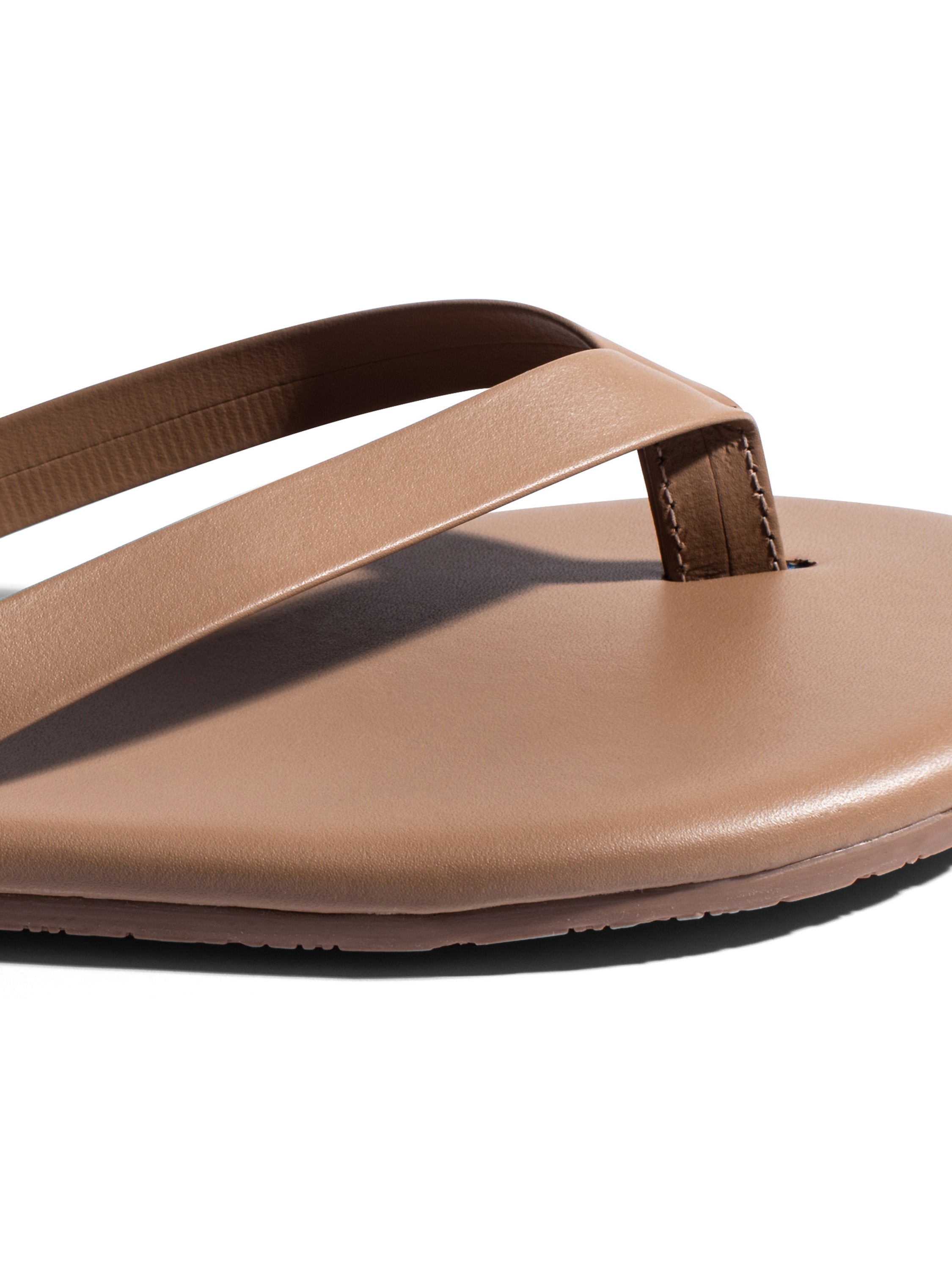 Minimalist tan leather flat thong sandals feature wide straps, a smooth footbed, and a subtly stitched toe post.