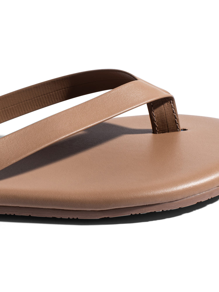 Minimalist tan leather flat thong sandals feature wide straps, a smooth footbed, and a subtly stitched toe post.