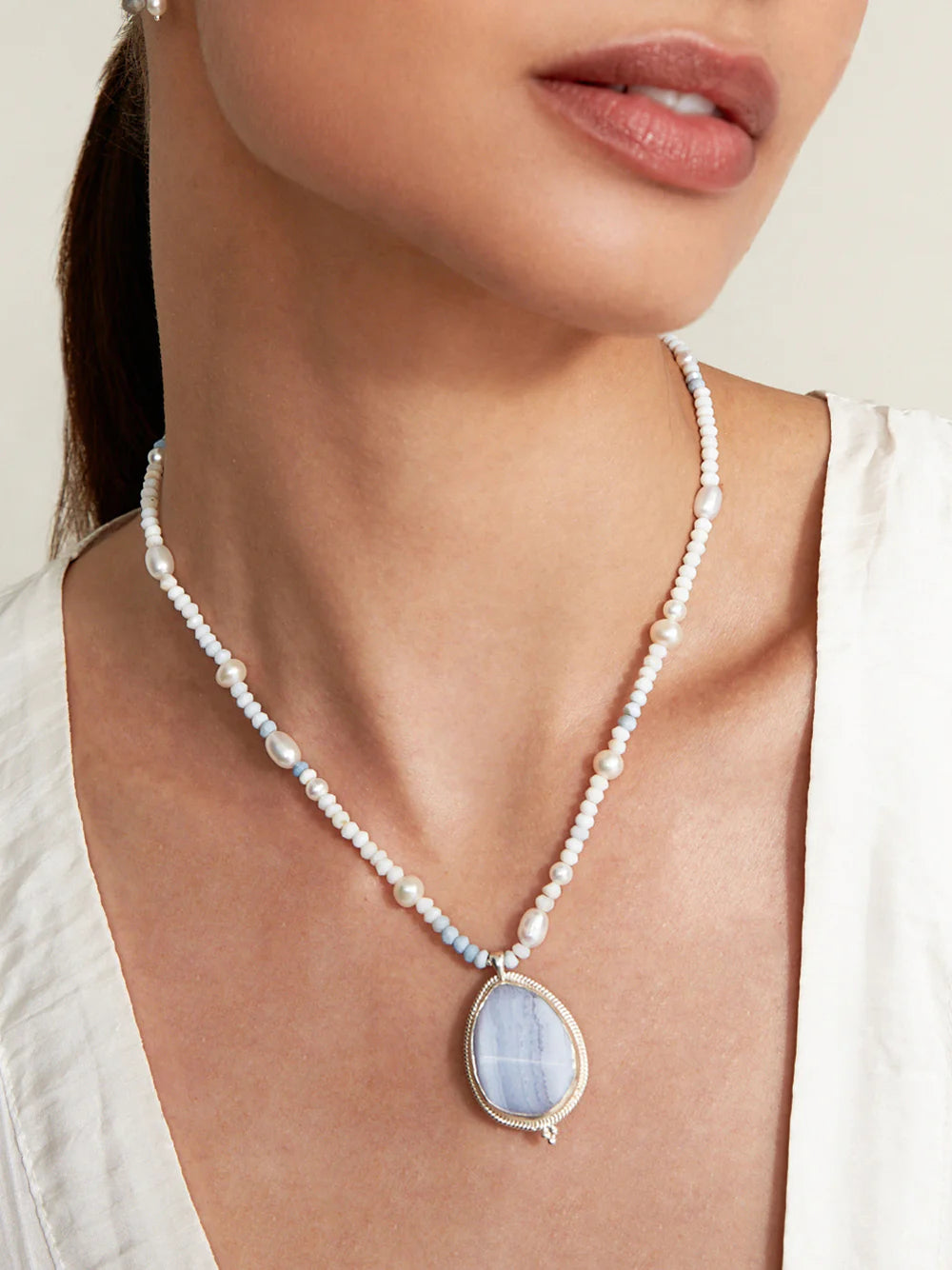 White pearl necklace with oval blue lace agate pendant in silver setting.
