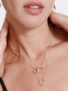 Silver double-strand necklace. One strand has two interlocking rings; the other has a horseshoe pendant with a clear stone.
