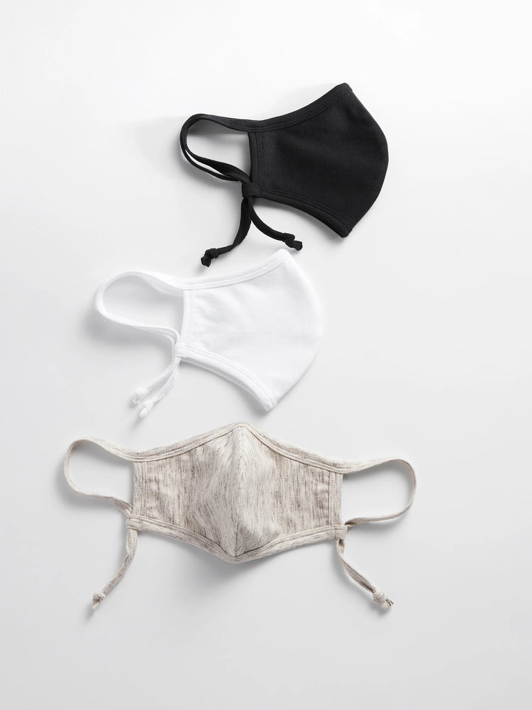Three fabric face masks: black, white, and heathered beige, with adjustable ear loops, laid flat.