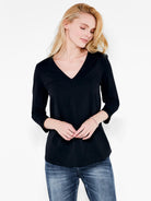 A blonde model wears a black v neck top with a regular fit and three quarter sleeves paired with blue jeans.