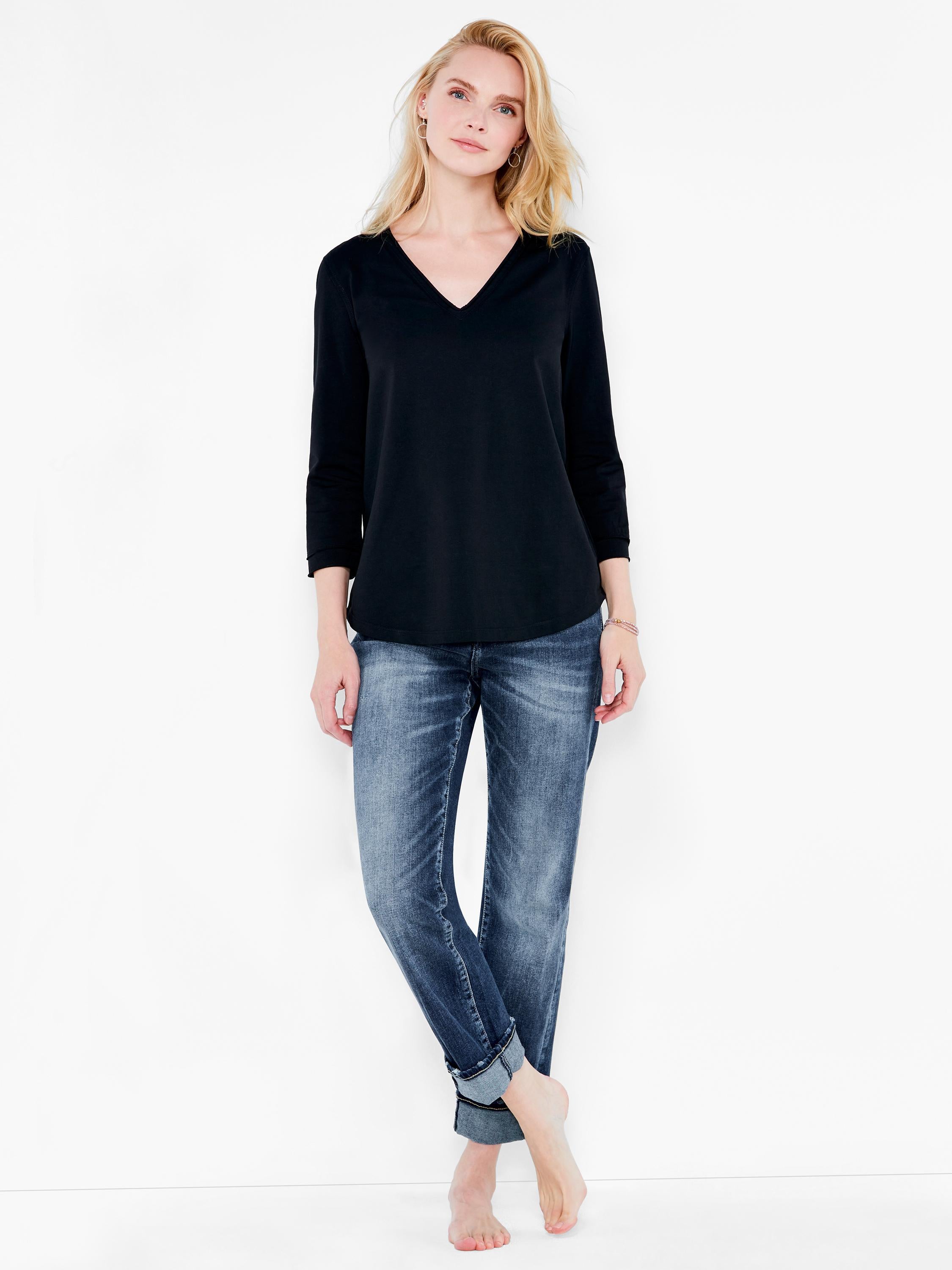 A loose black V-neck top with 3/4 sleeves and a slightly curved hem is worn with distressed cuffed blue jeans.