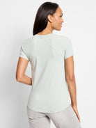 A woman wears a light green short sleeve crew neck tee with diagonal seams on the back.