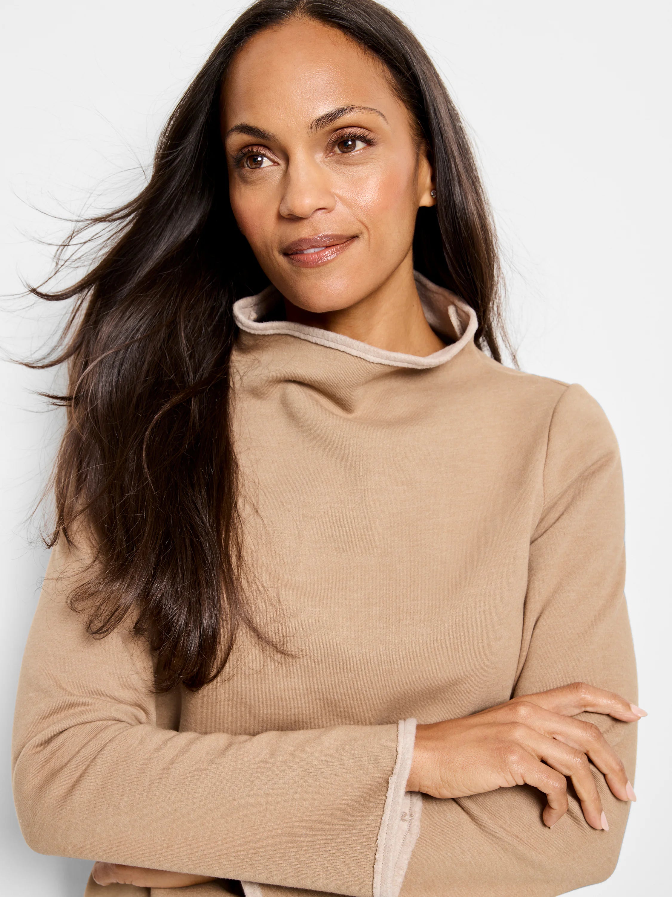 Beige long-sleeve top with lighter beige trim at the neck and cuffs. Mock neck. Model is wearing the top with arms crossed.