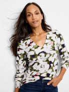 Long-sleeve V-neck top.  Off-white background with blurred green, dark purple, and pink floral pattern.