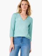 This mint green v neck top features three quarter sleeves and a relaxed fit, styled with blue jeans.