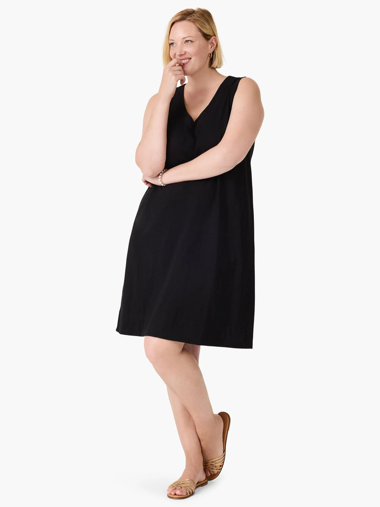 Black sleeveless V-neck dress, knee-length, A-line silhouette. Model is wearing gold sandals.