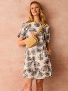 Off-white t-shirt dress with gray/teal leaf print, short sleeves, and pockets.  Model wears a tan woven belt bag.