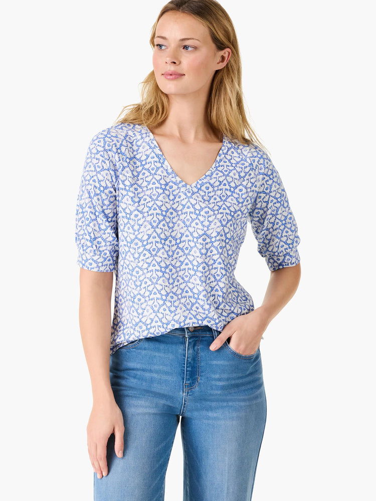 White v-neck shirt with blue ikat pattern, elbow-length sleeves.