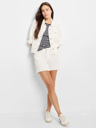 Off-white denim jacket with silver buttons, chest pockets, and frayed edges.