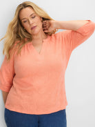 Peach top with a split V-neck, 3/4 sleeves, and an all-over subtle textured pattern.