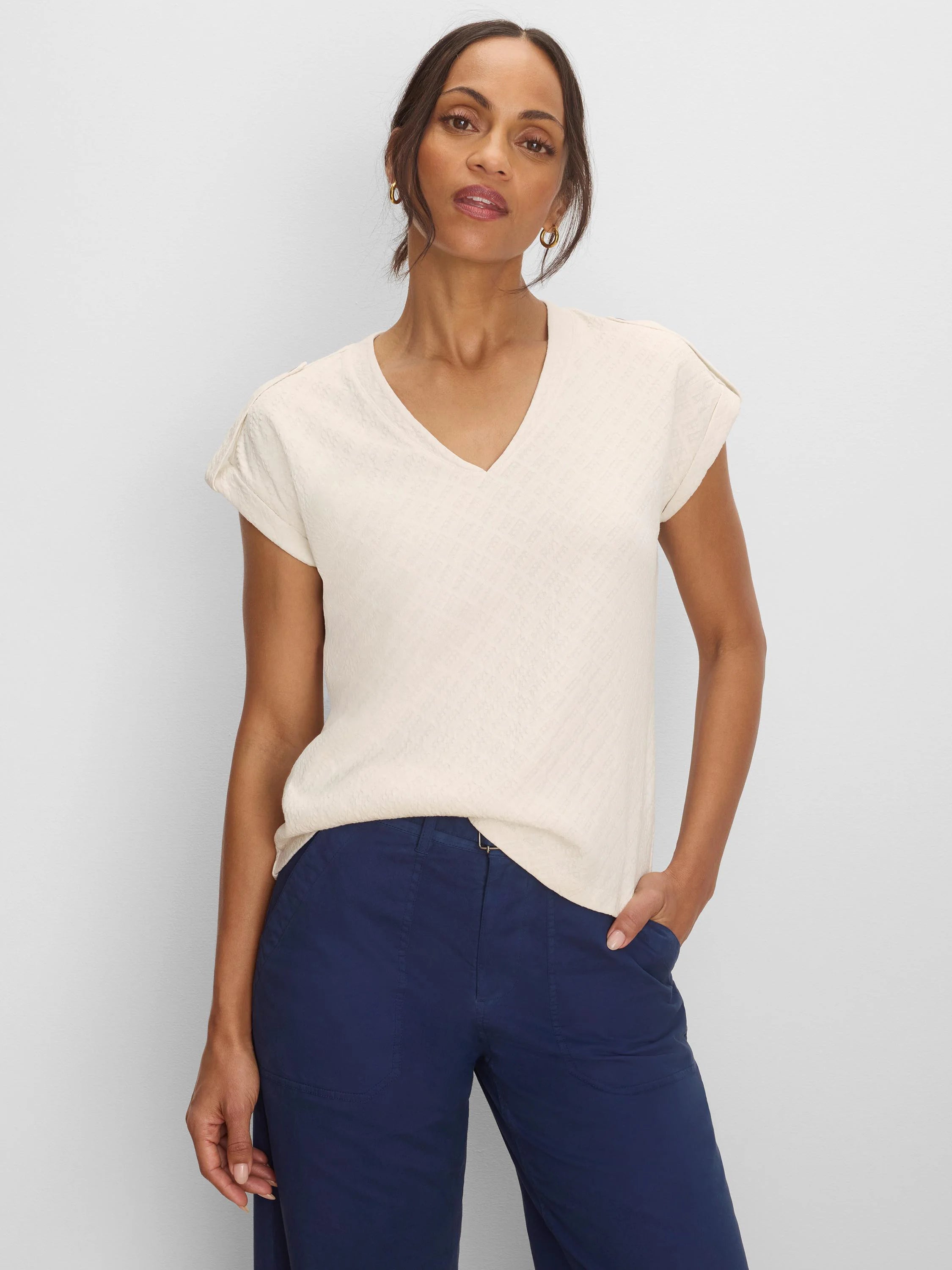 Light cream V-neck tee with subtle geometric lace knit texture and rolled cap sleeves.