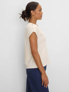 Off-white lace knit cap sleeve tee with buttoned shoulder tabs, worn by model.
