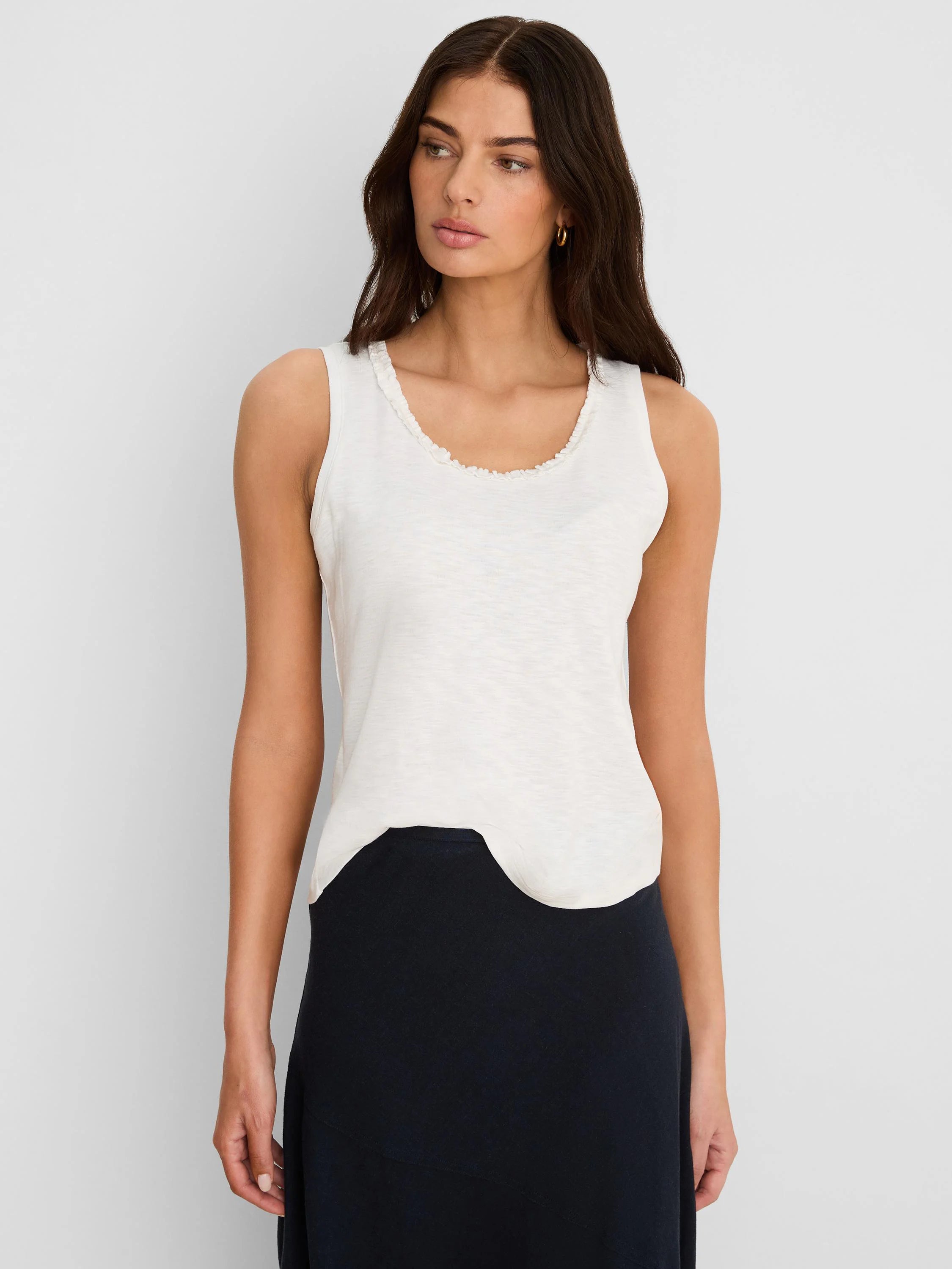 Off-white cotton slub tank top with ruffled neckline and curved hem.