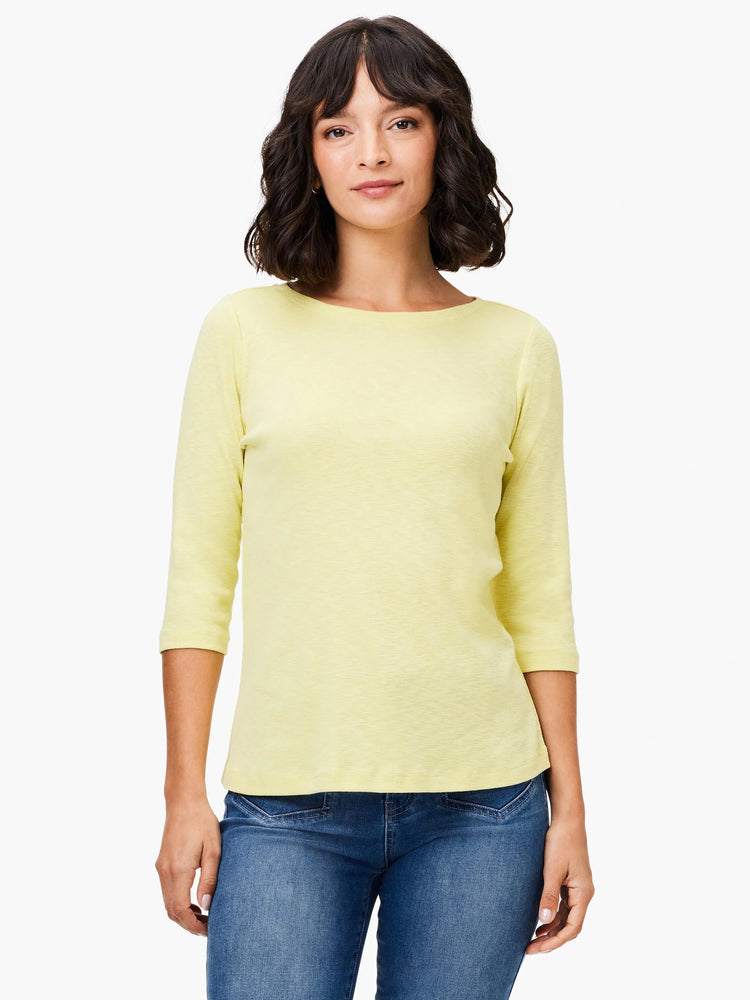 Woman wears a light yellow 3/4 sleeve boat neck tee with subtle texture, paired with blue jeans.