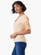 Peach-colored, short-sleeve top with ruched elbow sleeves and a split V-neck.