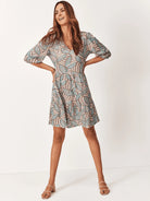 Beige mini dress with teal leaf pattern, elbow-length sleeves, and V-neck.
