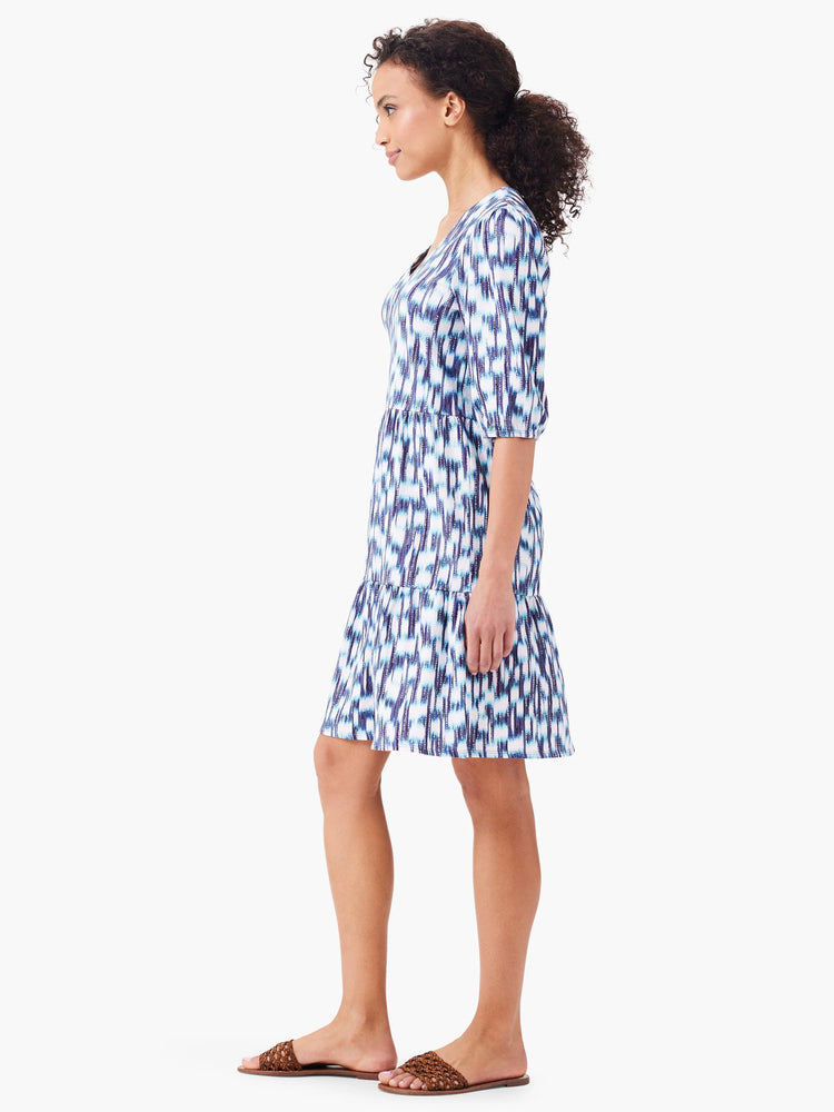 White tiered mini dress with blue and purple abstract print. Elbow-length sleeves, V-neck.